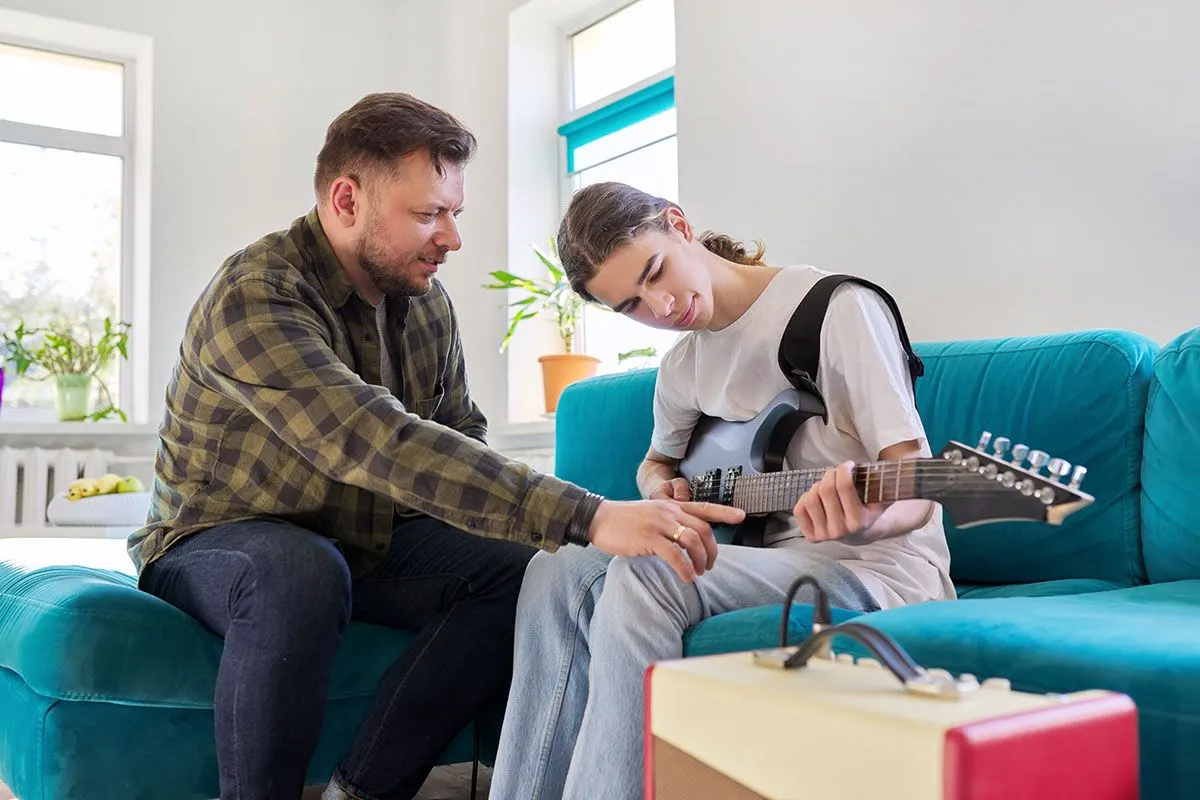 Adult helping a young person play an electric guitar
