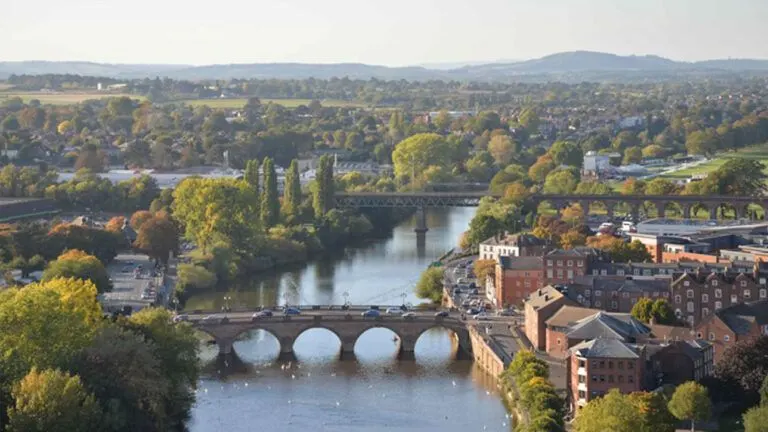 The image shows a panoramic view of Worcester, England, with the River Severn flowing through it and the city's bridges and buildings visible. Worcester and greater Worcestershire is an area served by Match Foster Care.