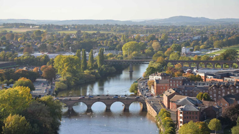 The image shows a panoramic view of Worcester, England, with the River Severn flowing through it and the city's bridges and buildings visible. Worcester and greater Worcestershire is an area served by Match Foster Care.
